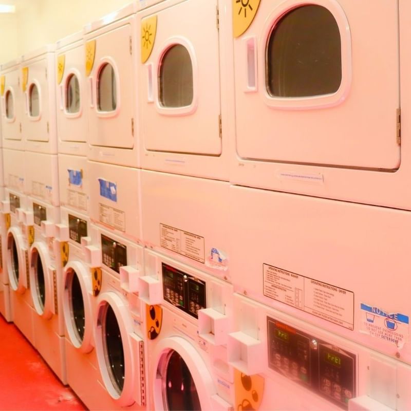 Multiple white washers and dryers in a clean, red-floored laundry room.