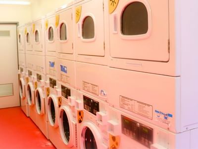 Multiple white washers and dryers in a clean, red-floored laundry room.