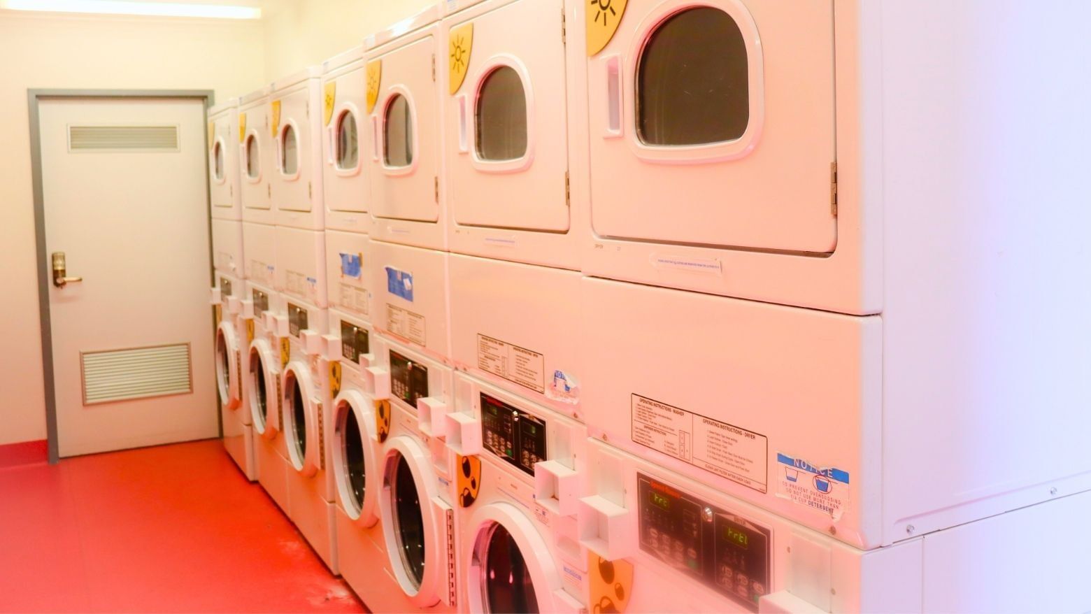 Multiple white washers and dryers in a clean, red-floored laundry room.