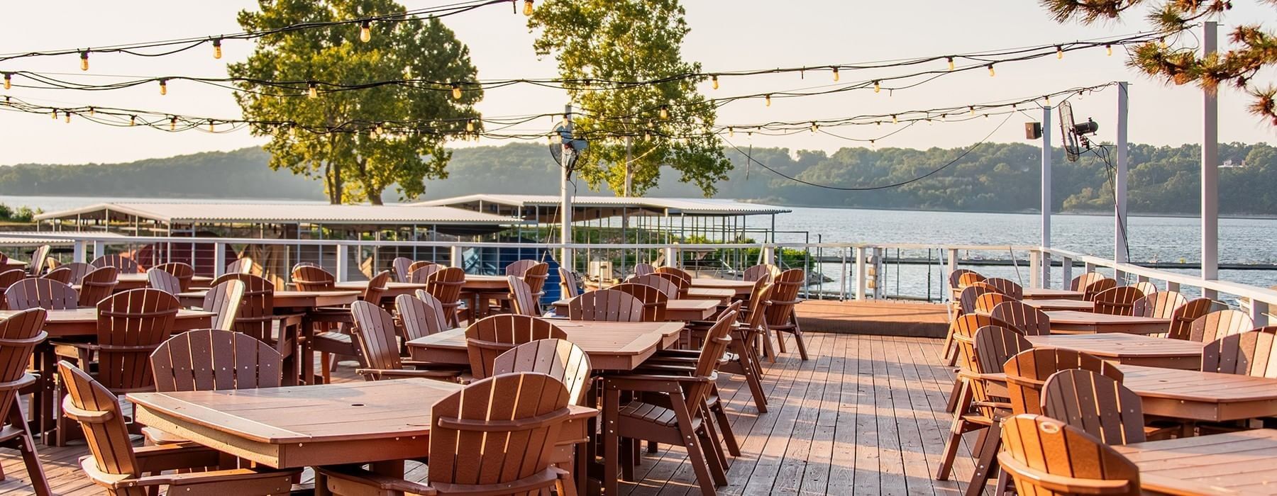 Wooden tables and chairs on a resort patio deck at sunset with a lake in the distance at Shangri-La Resort and Golf Club