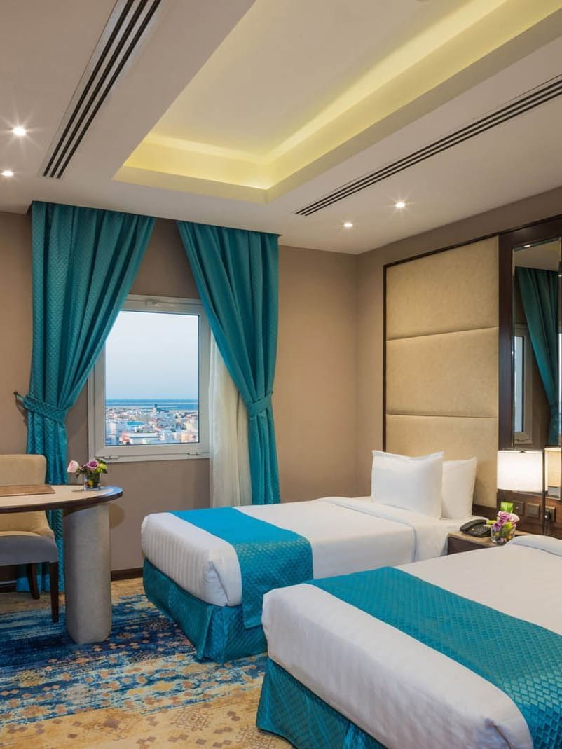 Two twin beds and a working desk near the window in the Junior Suite at Naviti By Warwick Dammam