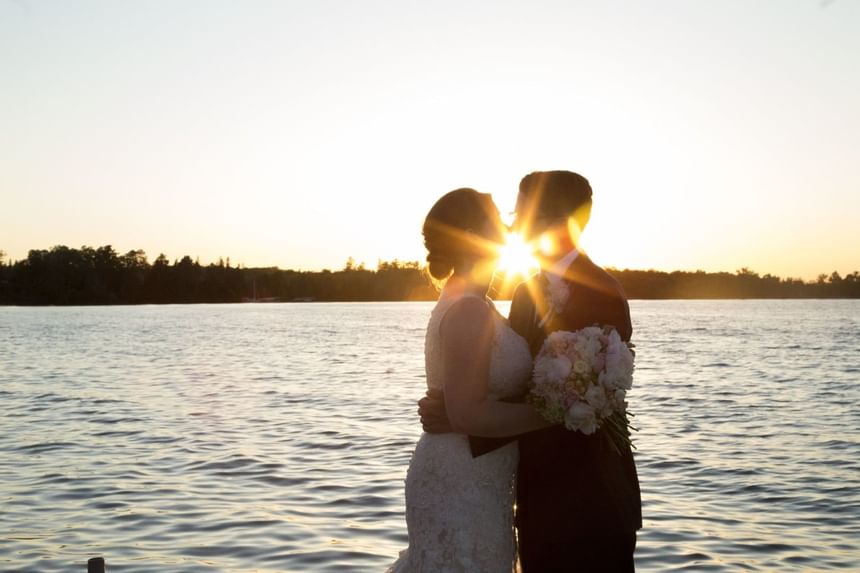 Wedding couple kissing while being bathed in the light of a sunset  over the lake. 