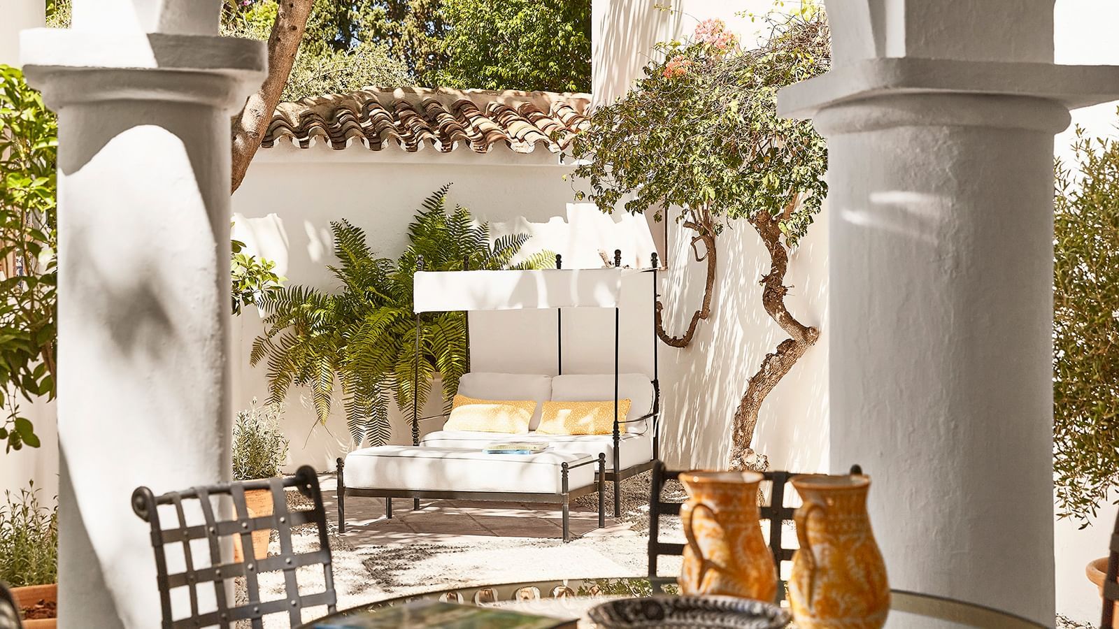 Outdoor daybed with yellow cushions under a pergola, placed in a sunny white courtyard at the Marbella Club