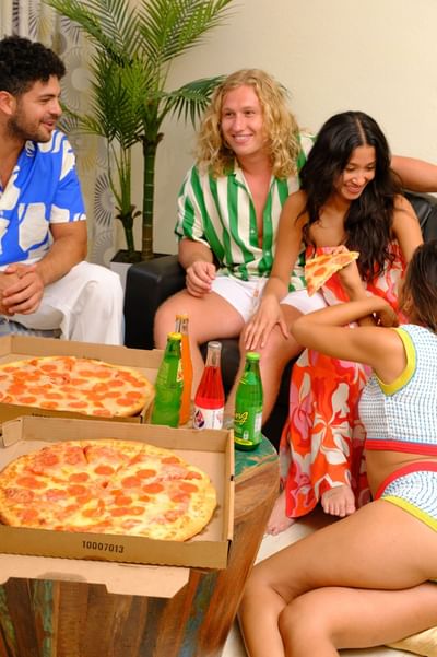Group of friends enjoying a pizza party and bottled drinks in their apartment living room at Tradewinds Apartment Hotel