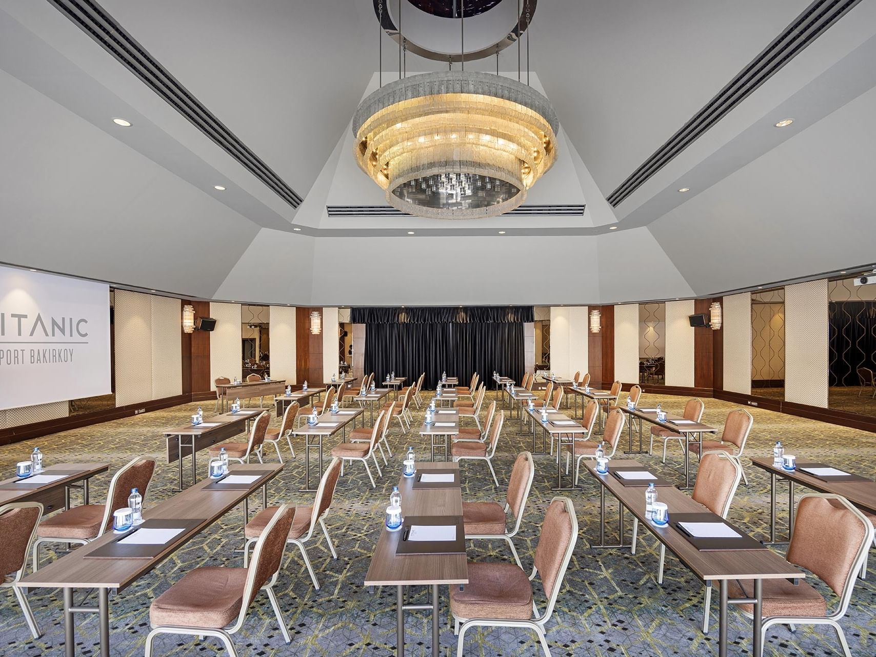 Adriatic toplantı salonunda sınıf düzeninde masa kurulumu, sandalyeler, su şişeleri ve projeksiyon perdesi Titanic Port Bakırköy’de.