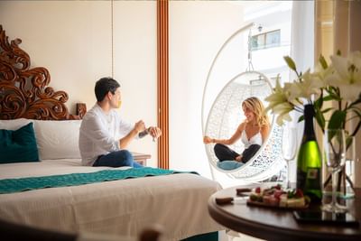 Couple relaxing in the guest room with carved headboard and hanging chair at Casa Dona Susana
