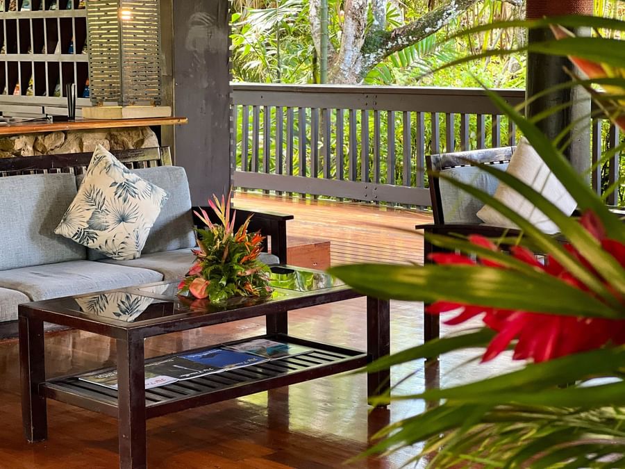 Wooden deck with a couch, glass table, and tropical flowers at The Naviti Resort Fiji.
