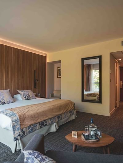 Chambre d'hôtel luxueuse avec lit, table, fauteuil, bureau, et miroir montrant un autre lit.