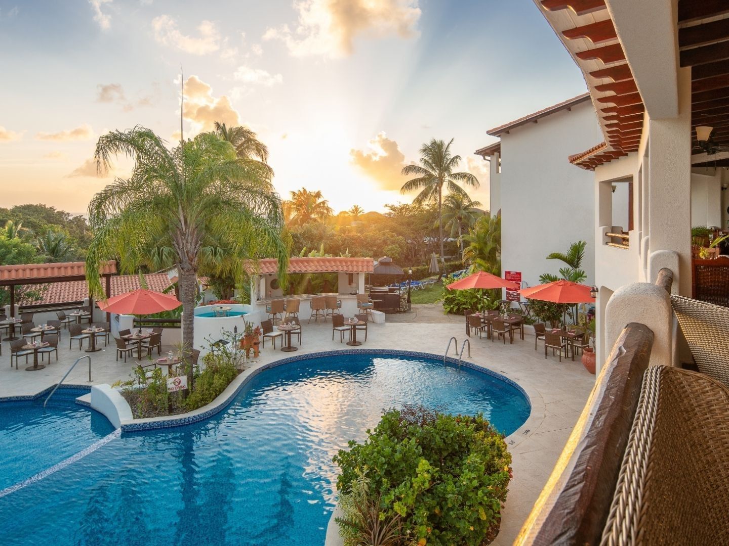 Outdoor dining tables and orange umbrellas by a swimming pool at sunset in Sugar Cane Club Hotel & Spa