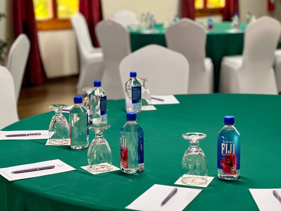 Round green tables with water bottles and pens by white chairs in a ballroom at TokaToka Resort Nadi Fiji