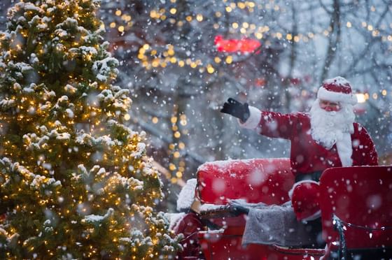 Santa posing on his sleigh by a snowy Christmas tree near Blackcomb Springs Suites