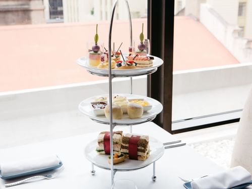 Three-tiered afternoon tea stand filled with sandwiches, and desserts in Restaurant Cuvée at Sofitel Brisbane Central
