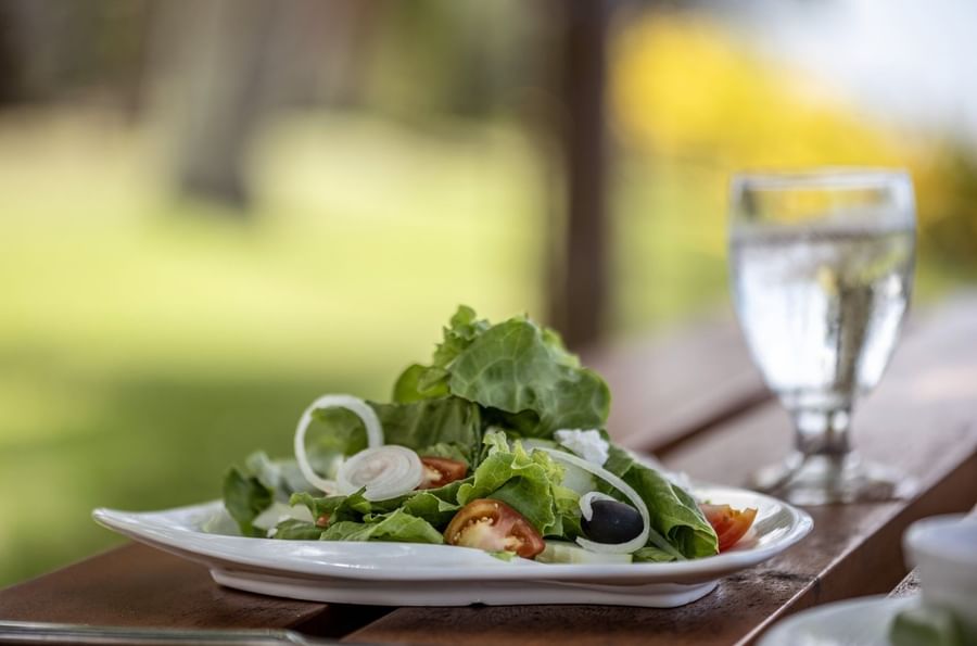 Fresh green salad with tomatoes & olives on a white plate by a water glass in Tambua Restaurant at Tambua Sands Beach Resort