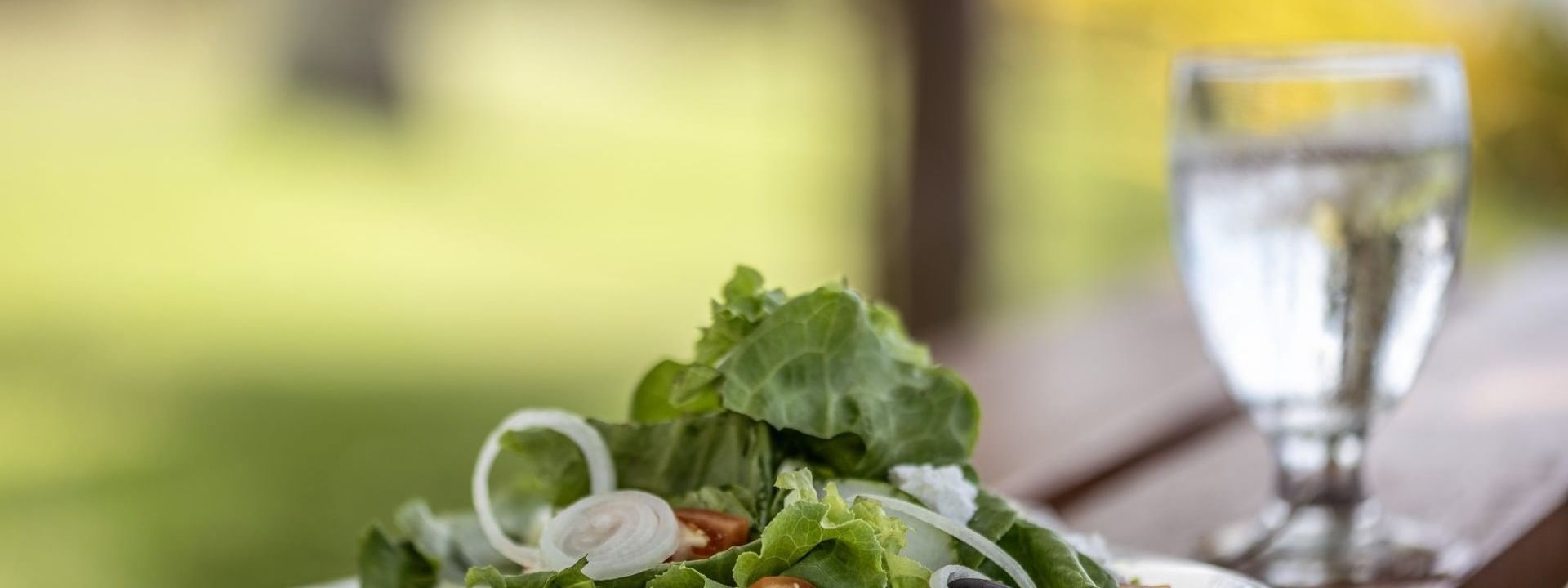 Fresh green salad with tomatoes & olives on a white plate by a water glass in Tambua Restaurant at Tambua Sands Beach Resort