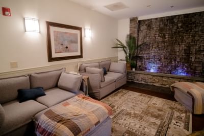 Spa relaxation room with plush grey sofas facing an illuminated stone waterfall wall at La Tourelle Hotel and Spa