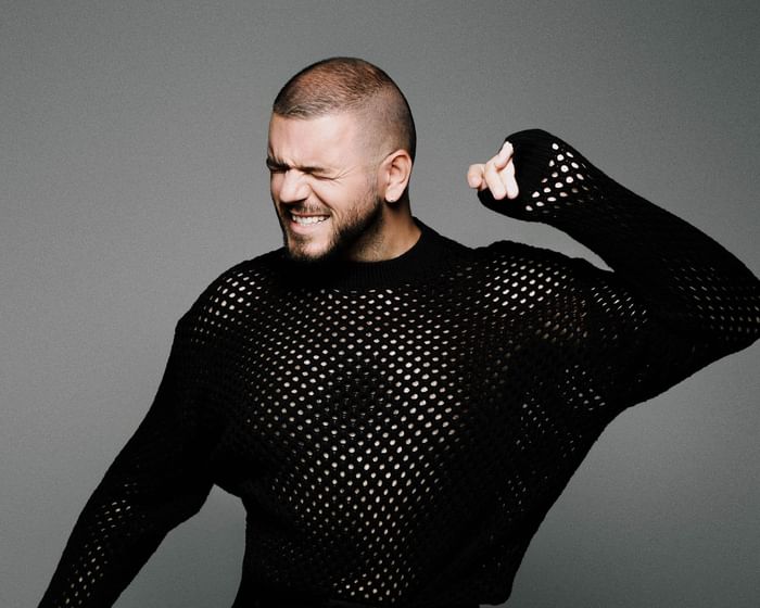 Photographer Stefan Kokovic in a black netted sweater posing dramatically against a gray backdrop at Hotel Motto Vienna