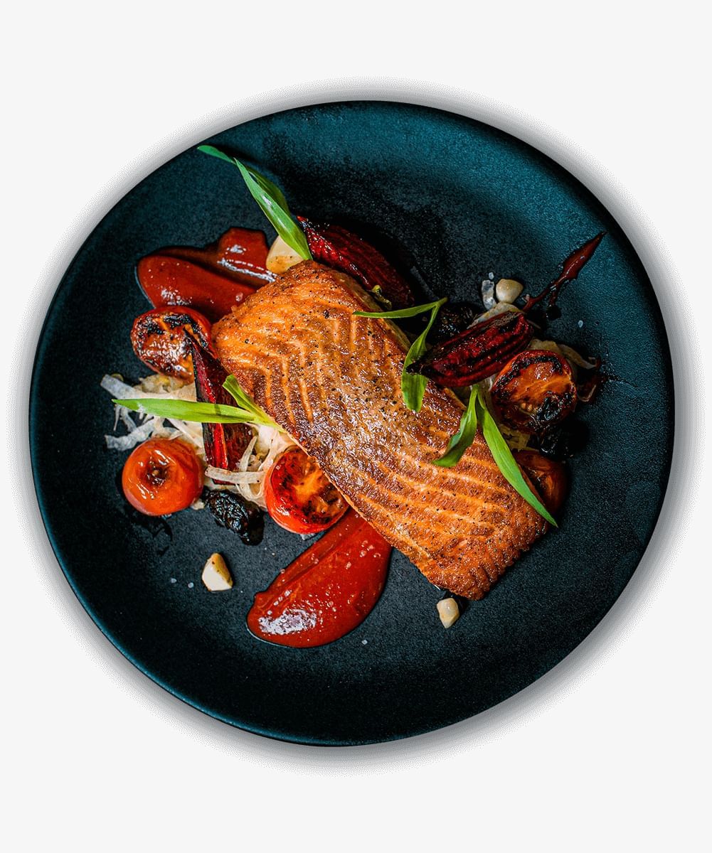 A plated dish of fish and vegetables on a black plate.