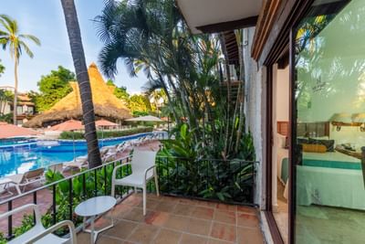 Balcony with white chairs and table, overlooking a pool and lush tropical surroundings.