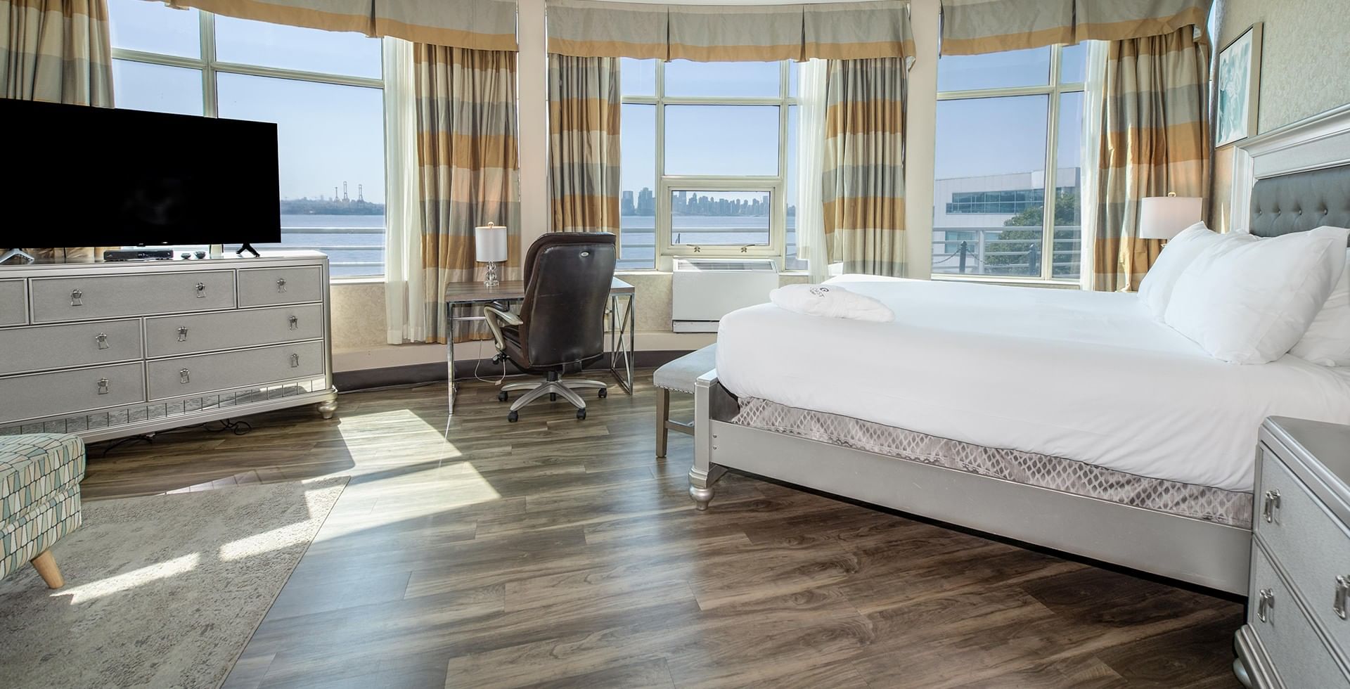 Luxurious hotel room with a white king-size bed, a desk, and expansive windows facing the water at Coast Lonsdale Quay Hotel