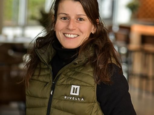Femme souriante portant un gilet vert avec logo Rivella.