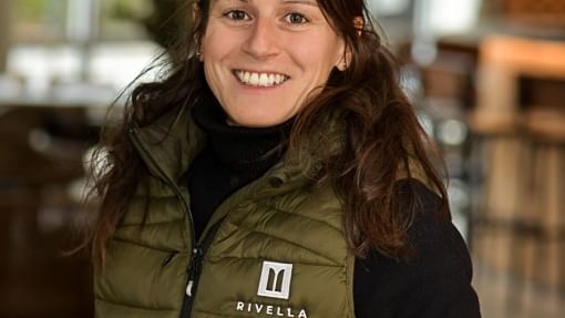 Femme souriante portant un gilet vert avec logo Rivella.