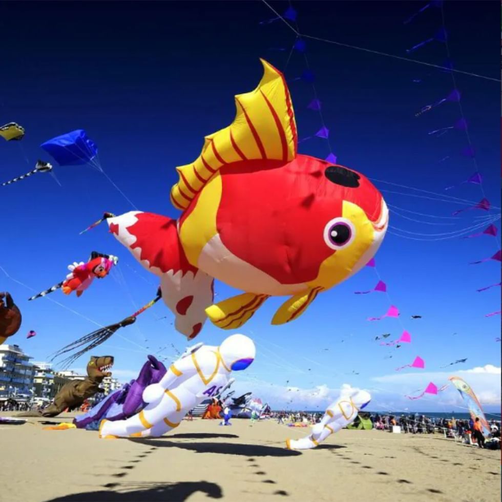 Large fish kite flying in the sky among various kites in a jesolo beach kite festival near Falkensteiner Hotel & Spa Jesolo