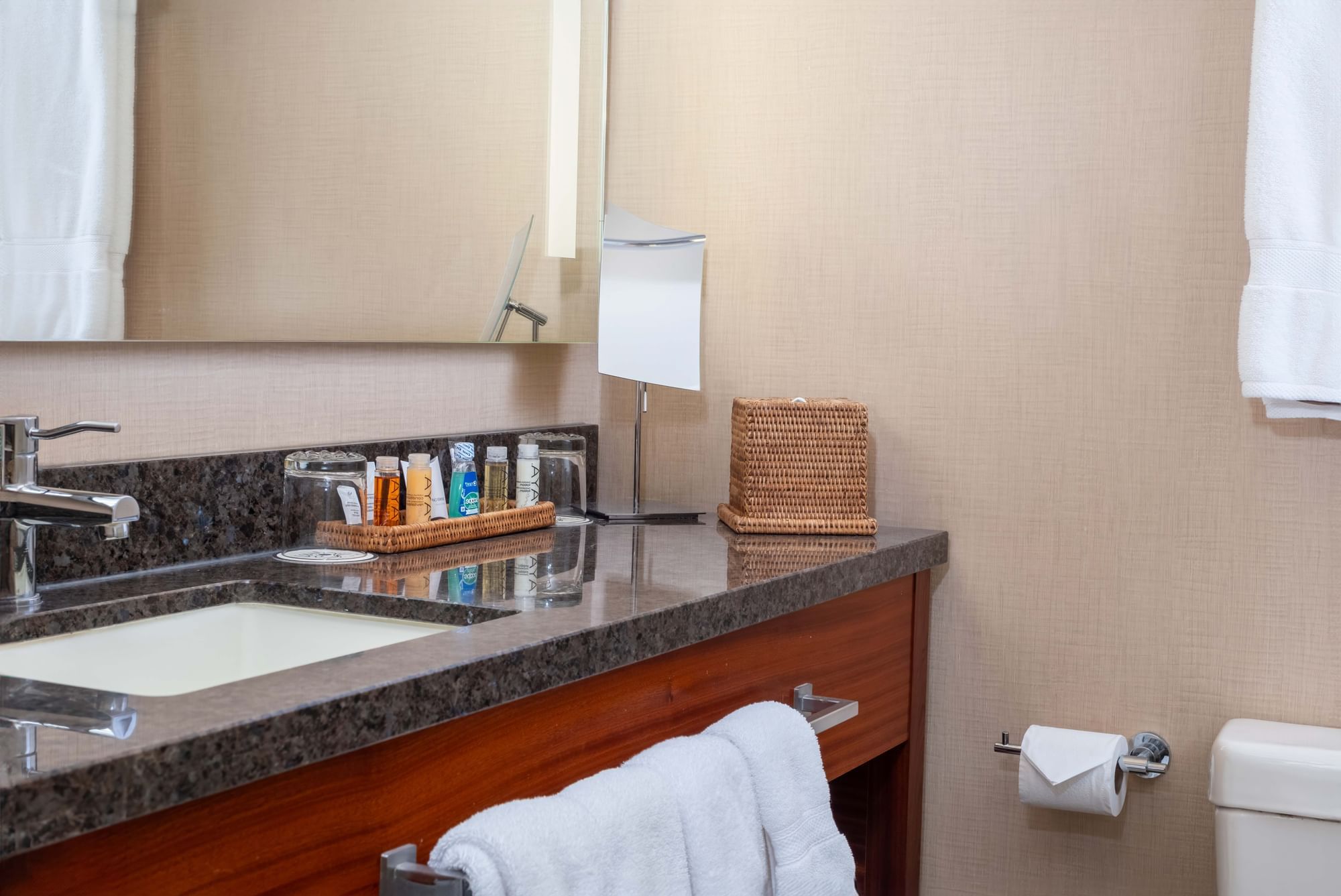 A bathroom sink area with a granite countertop, wooden cabinet, and toiletries.