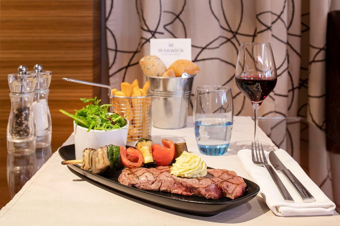 Plated beef entrecote with garlic butter, veggies, fries, and a glass of red wine served at Téséo Restaurant in Geneva