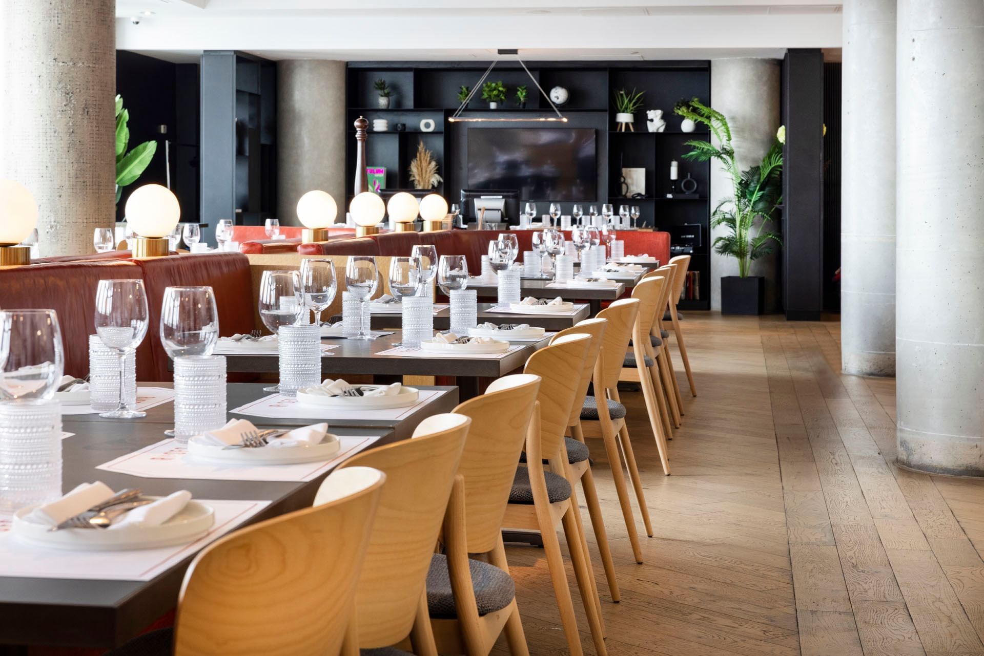 Roses restaurant dining area with long tables set with wine glasses and wooden chairs near leather booths at Hotel X Toronto