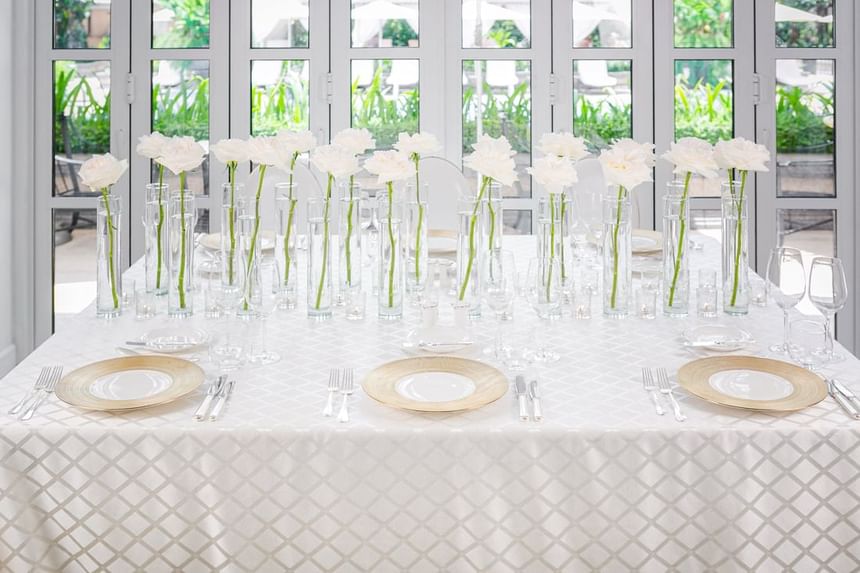 Table with a gold plate, white napkin, and tall glass vases of white flowers at Park Hyatt Saigon