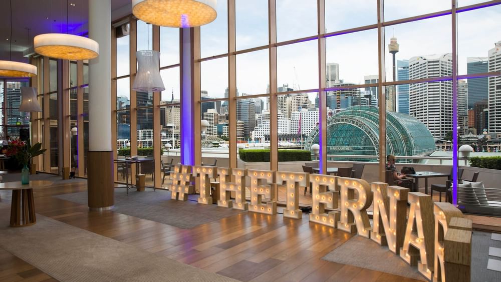 Lounge area with city views and a large illuminated sign in Events by The Ternary at Novotel Sydney on Darling Harbour