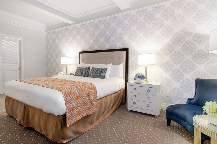 Premier Room featuring a patterned accent wall with large bed beside table lamp and blue chair at Warwick New York