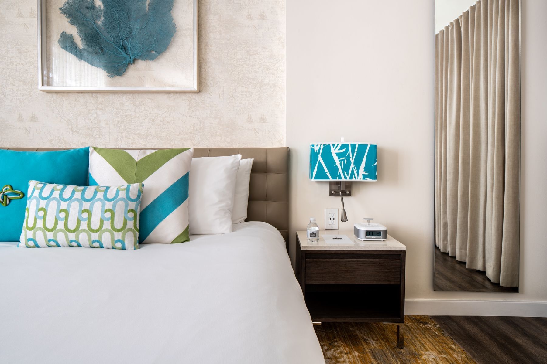 A hotel room with a bed, nightstand, lamp, and artwork on the wall.