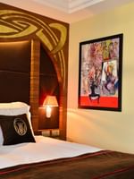 Deluxe Room features Bed with brown pillows by a colorful painting under a gold headboard at Warwick Ankara