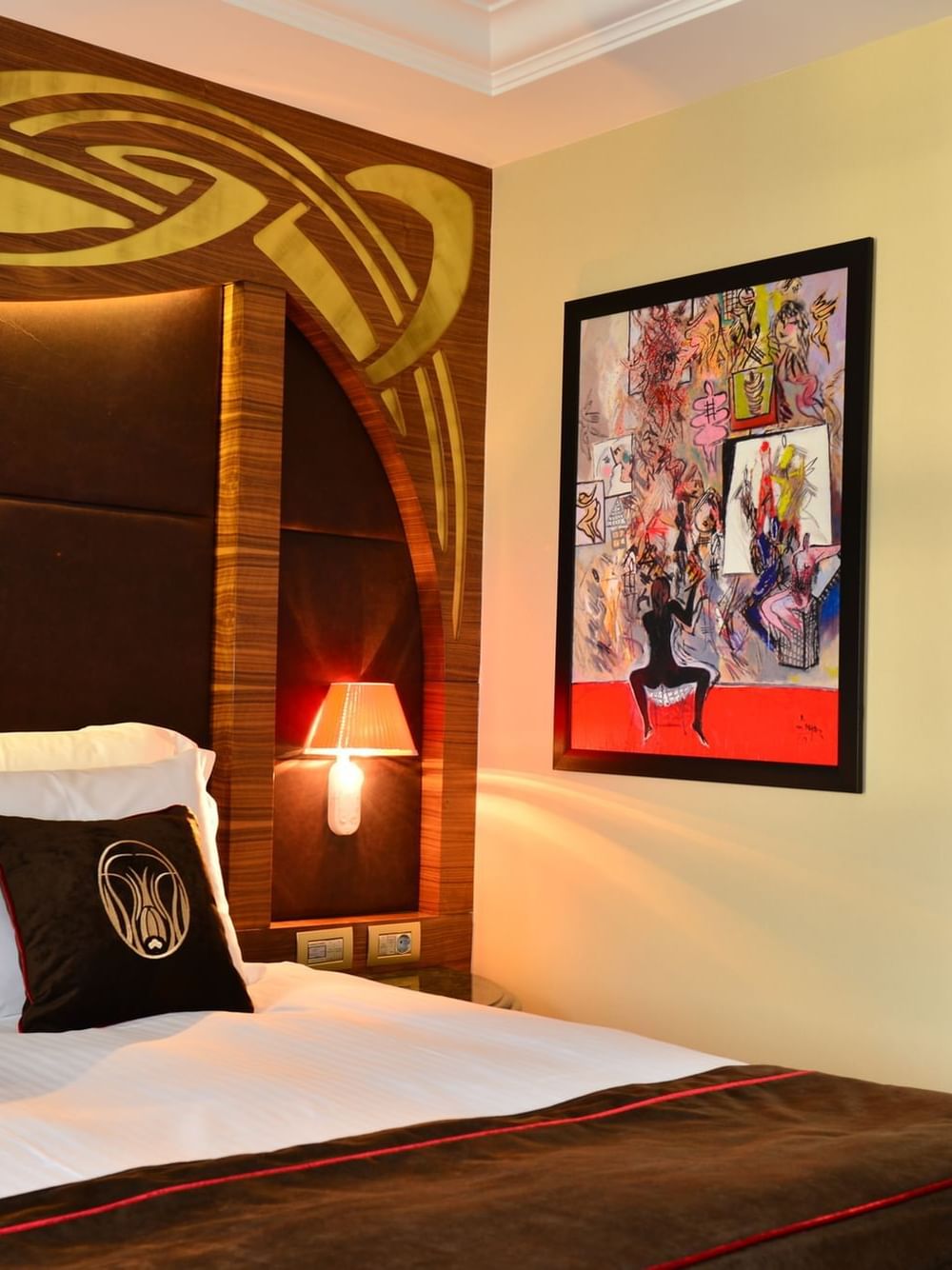 Deluxe Room features Bed with brown pillows by a colorful painting under a gold headboard at Warwick Ankara