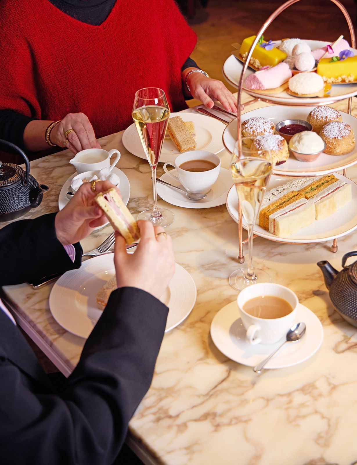 People enjoying a three-tier afternoon tea spread with teacups and pastries in May Fair Kitchen