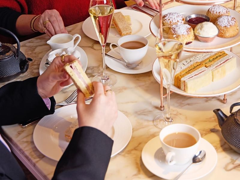 People enjoying a three-tier afternoon tea spread with teacups and pastries in May Fair Kitchen