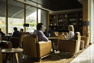 Huéspedes en sillones de cuero junto a mesas de madera bajo techo oscuro alrededor de un bar en NOI Vitacura