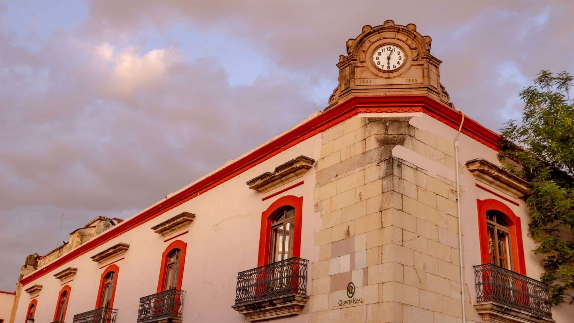 Esquina blanca del hotel con marcos de ventana rojos y reloj vintage en Quinta Real Oaxaca