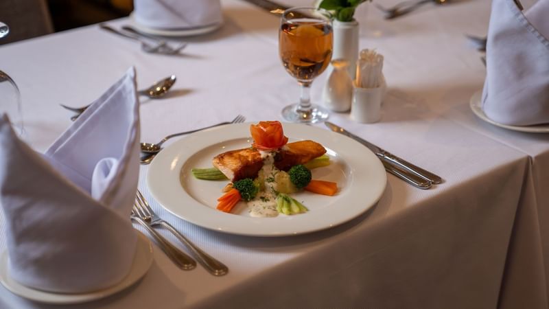 Plate of seafood, vegetables, and white sauce with cutlery and wine glass at Saja by Warwick Madinah.
