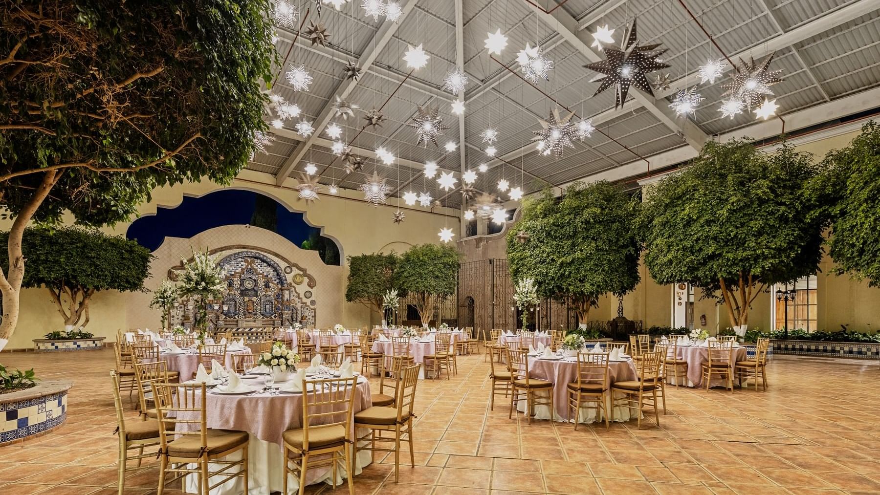 Outdoor event space at Fiesta Americana, adorned with star-shaped lights, lush trees, and elegantly set round tables