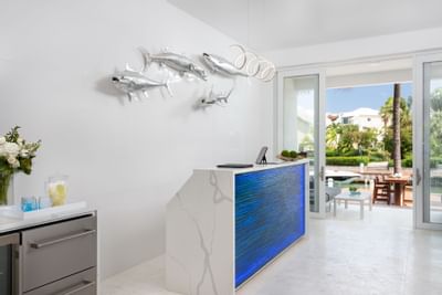 Minimalist white marble reception desk with a glowing blue front and silver metal fish wall sculptures at Zenza Hotel