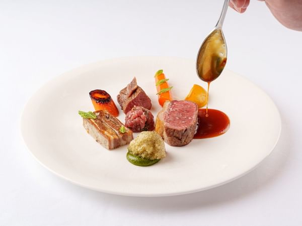 Hand pouring sauce over a plate of food at The Capital Hotel, Apartments & Townhouse - London.