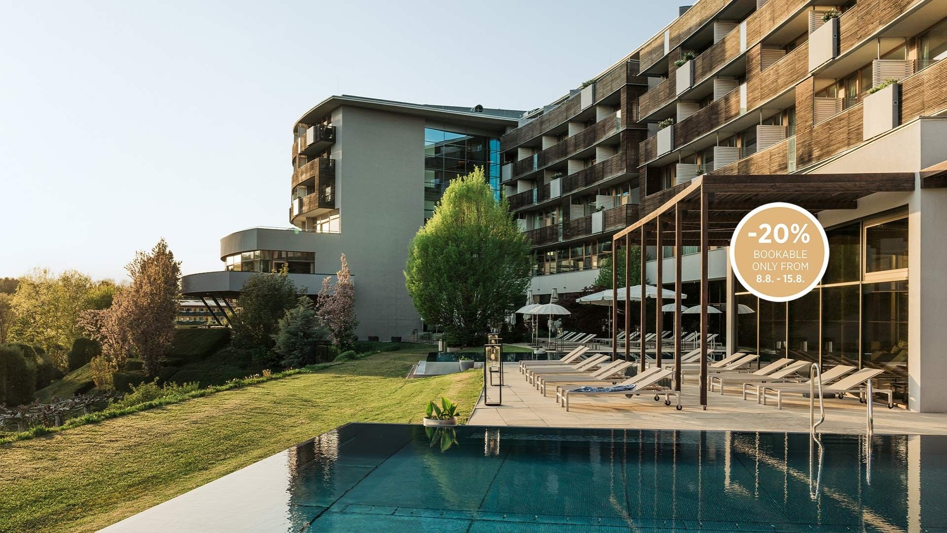 Hotel moderno con piscina e lettini, circondato da alberi e prati verdi, con offerta del -20%.