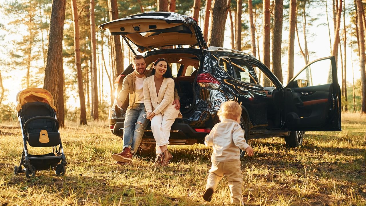 Couple and child by car with stroller, smiling and posing in a forest setting.