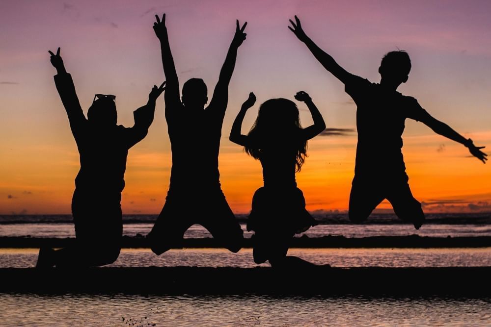 The silhouettes of four people jumping joyously in front of a beach at sunset.