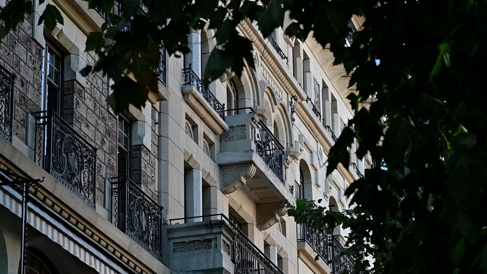 Hotel exterior featuring ornate stone balconies under green leaves by large windows near Warwick Geneva