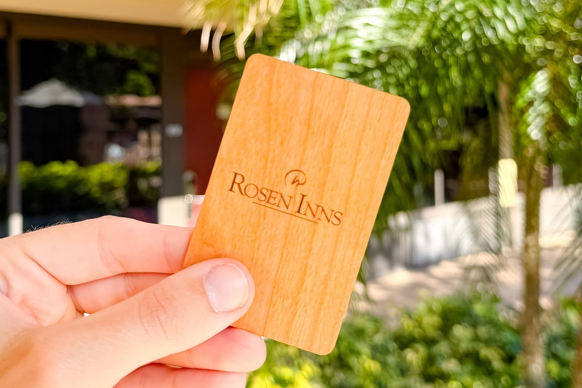 A close-up of a hand holding a wooden Rosen Inns room key. 