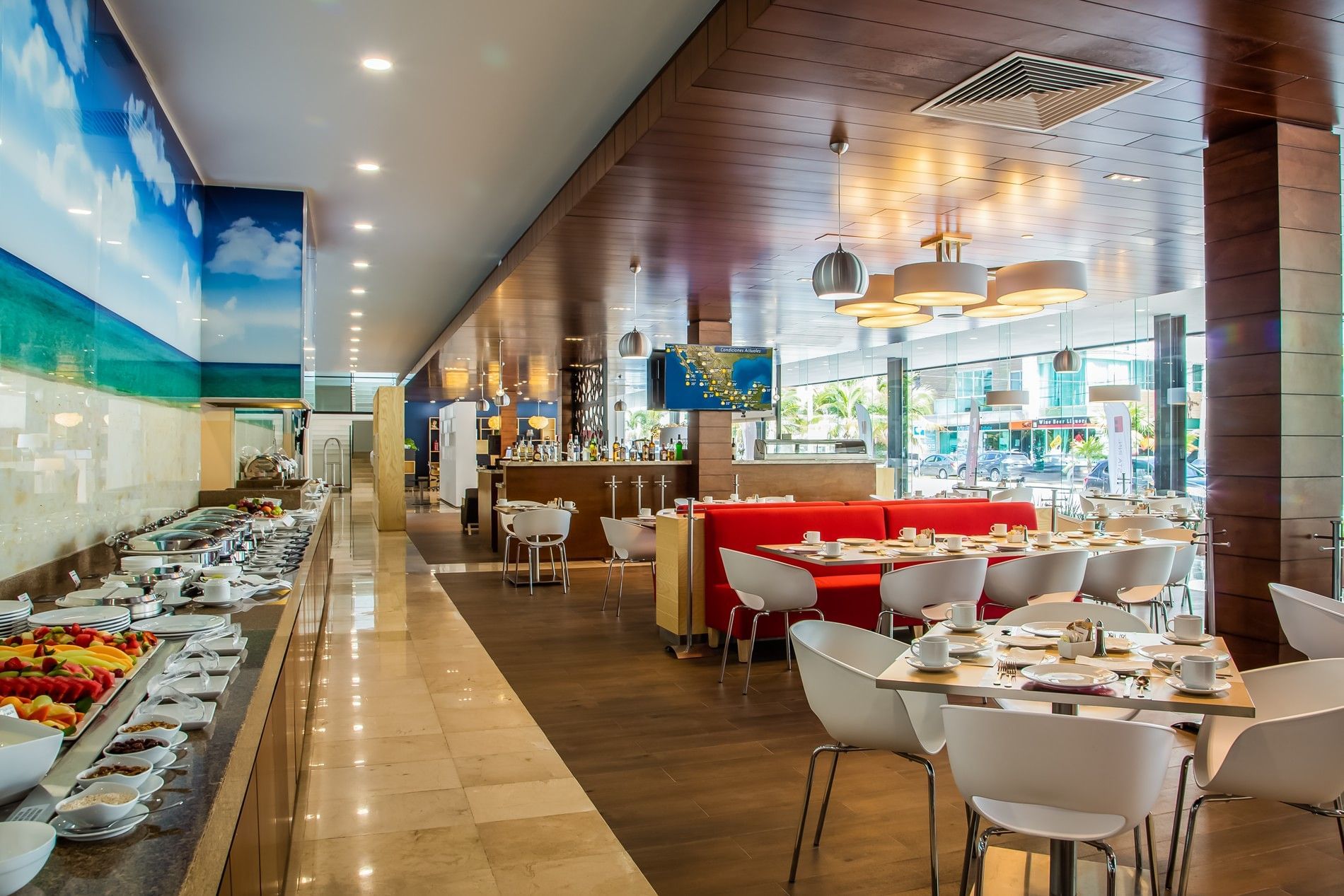 Área de comedor moderna del hotel con línea de buffet y mural tropical vibrante en Fiesta Inn