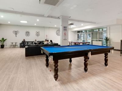 People sitting on couches and playing pool in a room at La Trobe University – Menzies College.